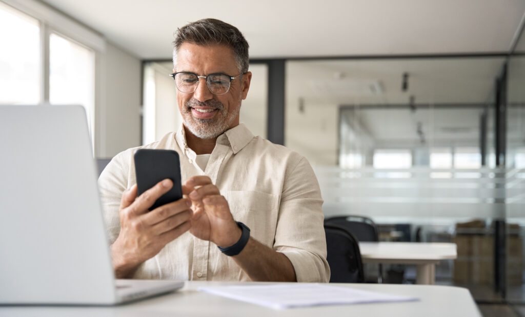 Middle aged Hispanic business manager ceo using cell phone mobile app, laptop.