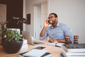 Shot of happy black man sitting at table and talking on mobile phone.