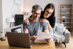 Couple at home on their laptop and looking at paper documents