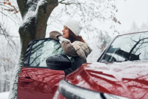 Walking out off car. Young woman is outdoors near her red automobile at winter time.
