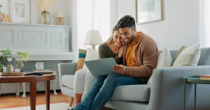 Young couple sitting on couch in home looking at something on their laptop