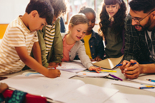 Group of children doing an art project with their teacher. Elementary school students enjoy drawing using coloring pencils. Creativity as part of early child development.